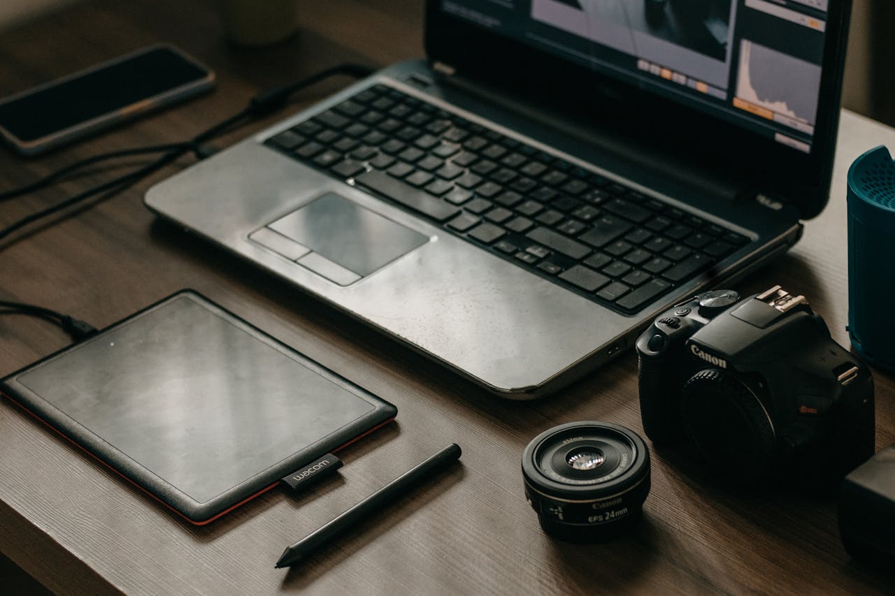 services-02 Laptop, camera, lens, and graphic tablet on a desk for digital creatives.