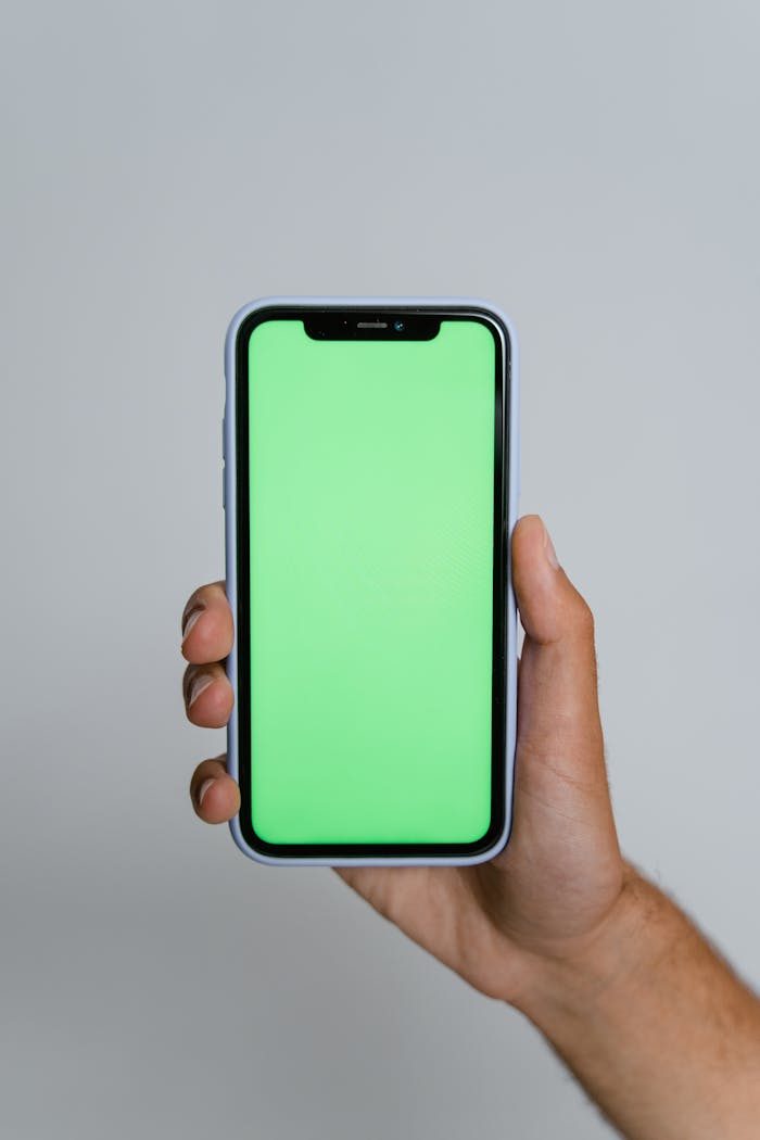 A close-up of a hand holding a smartphone with a vibrant green screen, ideal for mockups.